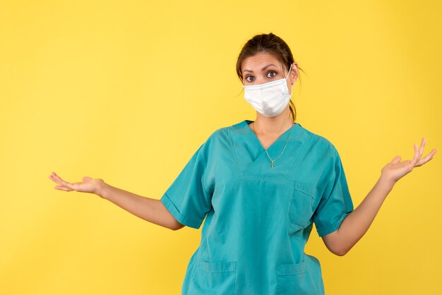 Vue de face femme médecin en chemise médicale et masque stérile sur fond jaune