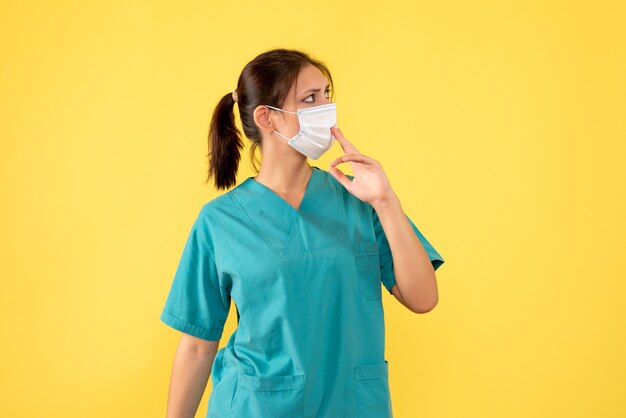 Vue de face femme médecin en chemise médicale et avec masque stérile sur fond jaune