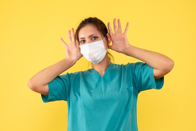 Vue de face femme médecin en chemise médicale et avec masque stérile sur fond jaune