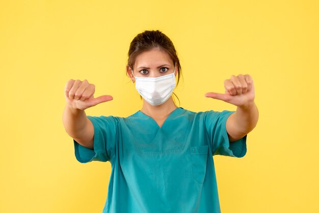 Vue de face femme médecin en chemise médicale et avec masque stérile sur fond jaune