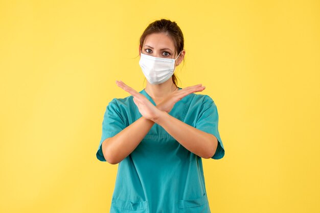 Vue de face femme médecin en chemise médicale et avec masque stérile sur fond jaune