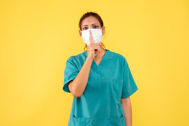Vue de face femme médecin en chemise médicale et avec masque stérile sur fond jaune