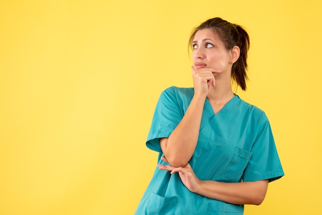 Vue de face femme médecin en chemise médicale pensant sur fond jaune