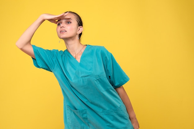 Vue de face femme médecin en chemise médicale à la recherche à distance sur bureau jaune couleur santé infirmière covid-19 émotion virus de l'hôpital