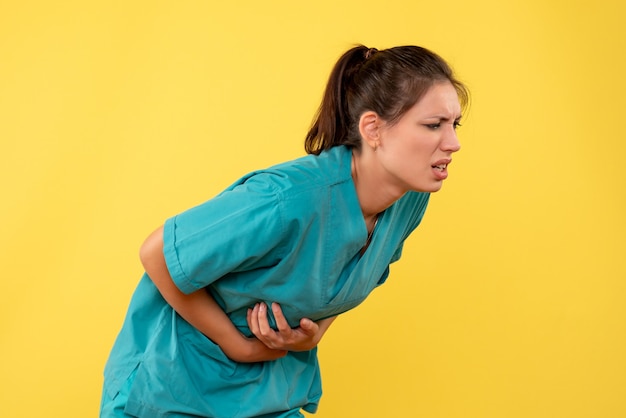 Vue de face femme médecin en chemise médicale souffrant de maux d'estomac sur fond jaune