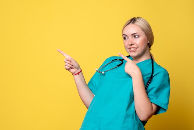 Vue de face de la femme médecin en chemise médicale avec stéthoscope sur mur jaune