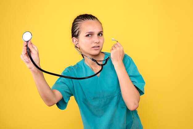 Vue de face de la femme médecin en chemise médicale avec stéthoscope sur mur jaune