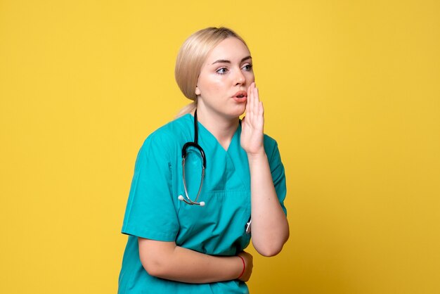 Vue de face de la femme médecin en chemise médicale avec stéthoscope sur mur jaune