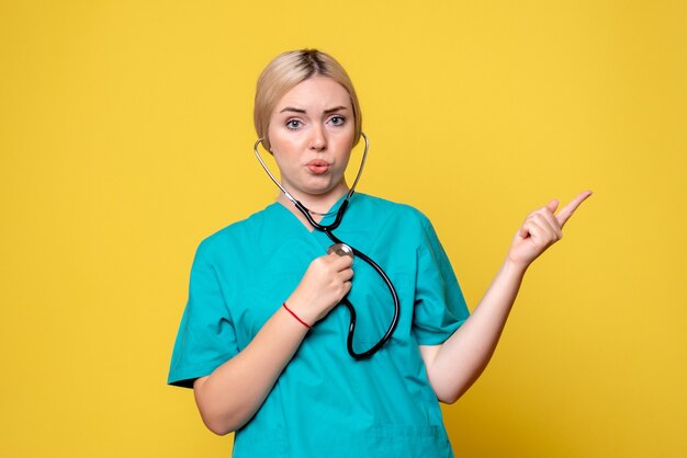 Vue de face de la femme médecin en chemise médicale avec stéthoscope sur mur jaune