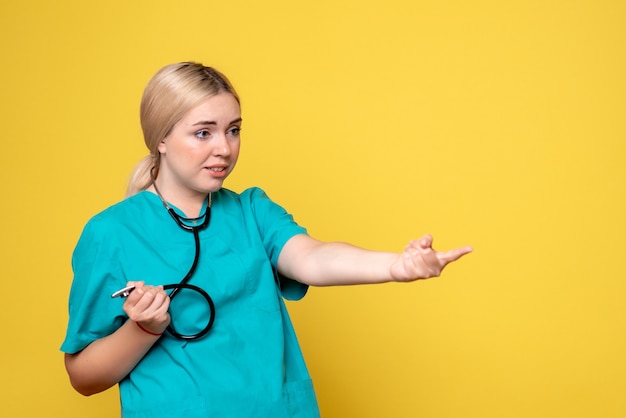 Vue de face de la femme médecin en chemise médicale avec stéthoscope sur mur jaune