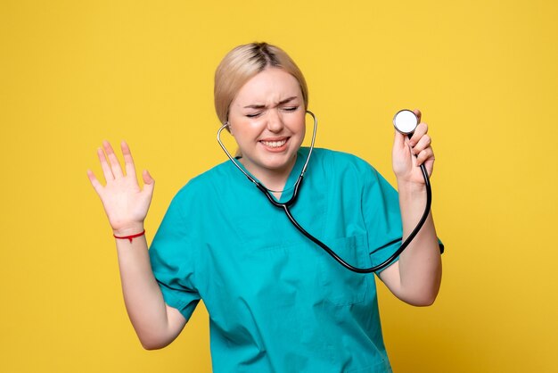 Vue de face de la femme médecin en chemise médicale avec stéthoscope sur mur jaune