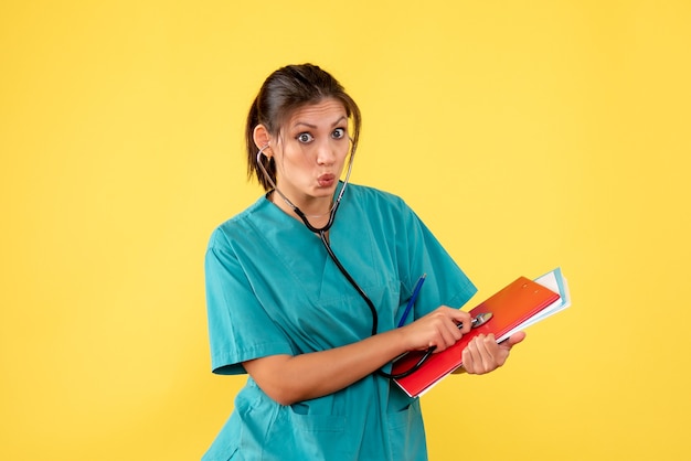 Vue de face femme médecin en chemise médicale avec stéthoscope et notes sur fond jaune