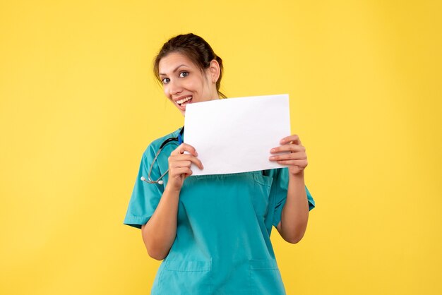 Vue de face femme médecin en chemise médicale tenant l'analyse du papier sur le bureau jaune medic virus couleur hôpital médecine de la santé