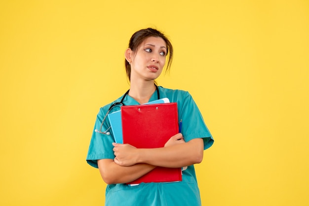 Vue de face femme médecin en chemise médicale tenant l'analyse sur fond jaune