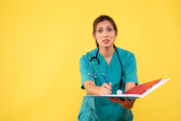 Vue de face femme médecin en chemise médicale tenant l'analyse sur fond jaune