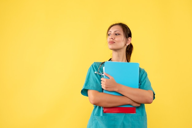 Vue de face femme médecin en chemise médicale tenant l'analyse sur fond jaune