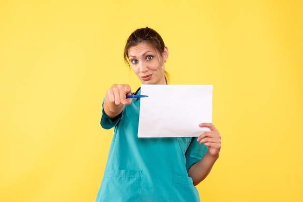 Vue de face femme médecin en chemise médicale tenant l'analyse de papier sur fond jaune