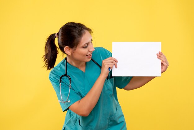 Vue de face femme médecin en chemise médicale tenant l'analyse de papier sur fond jaune