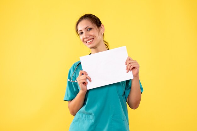 Vue de face femme médecin en chemise médicale tenant l'analyse de papier sur fond jaune