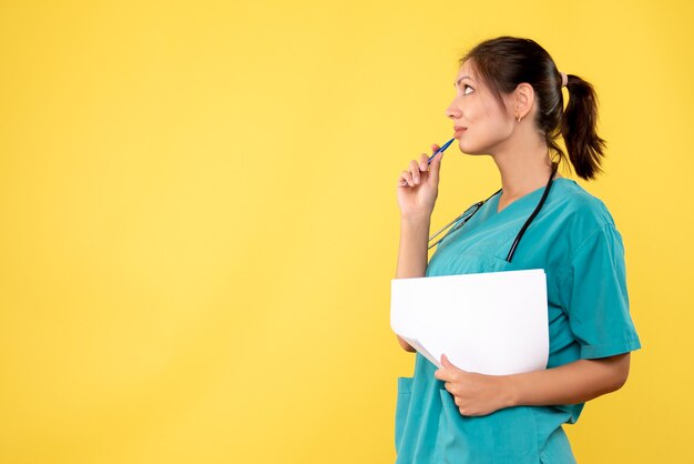Vue de face femme médecin en chemise médicale tenant l'analyse de papier sur fond jaune