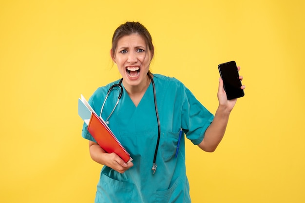 Vue de face femme médecin en chemise médicale tenant l'analyse et le téléphone sur fond jaune