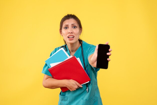 Vue de face femme médecin en chemise médicale tenant l'analyse et le téléphone sur fond jaune
