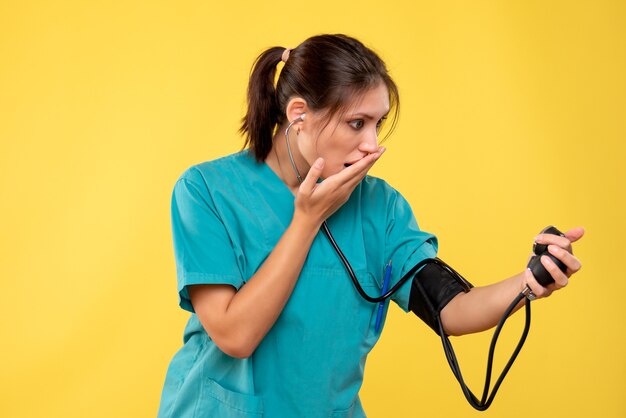 Vue de face femme médecin en chemise médicale vérifiant sa pression sur fond jaune