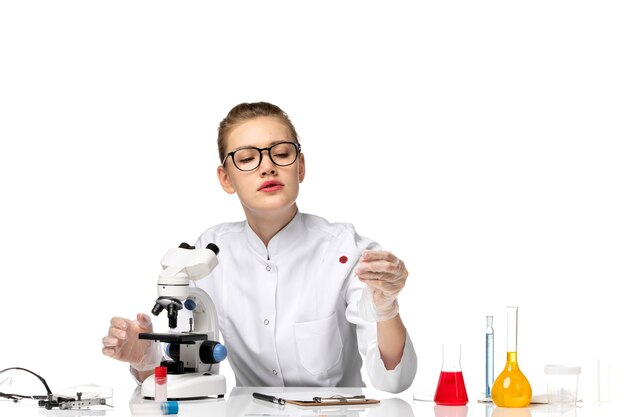 Vue de face femme médecin en combinaison médicale avec des gants en cours de travail sur un bureau blanc