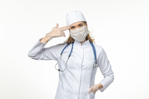 Vue de face femme médecin en combinaison médicale portant un masque et des gants en raison d'un coronavirus sur la maladie du virus de la maladie pandémique pandémique de bureau blanc