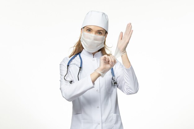 Vue de face femme médecin en combinaison médicale portant un masque et des gants en raison d'un coronavirus sur le mur blanc pandémie de maladie de covid