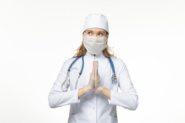 Vue de face femme médecin en combinaison médicale portant un masque avec des gants en raison d'un coronavirus sur le virus pandémique de la maladie de bureau blanc covid-