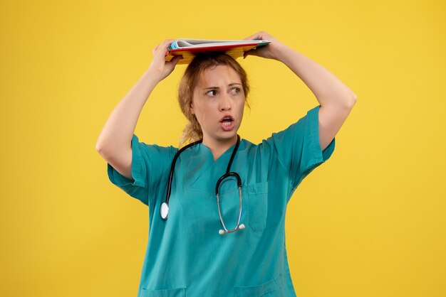 Vue de face de la femme médecin en costume médical avec analyse sur mur jaune