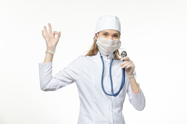 Vue de face femme médecin en costume médical blanc à l'aide d'un stéthoscope sur le bureau maladie covid- pandémie