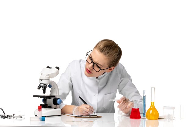 Vue de face femme médecin en costume médical blanc, écrire des notes sur l'espace blanc