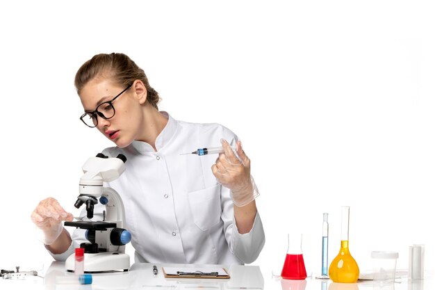 Vue de face femme médecin en costume médical blanc avec des gants à l'aide de l'injection sur un bureau blanc