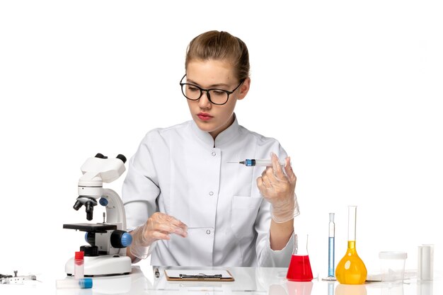 Vue de face femme médecin en costume médical blanc avec des gants à l'aide de l'injection sur l'espace blanc