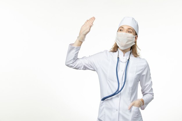 Vue de face femme médecin en costume médical blanc et masque comme protection contre le coronavirus sur la maladie du plancher blanc covid- maladie pandémique