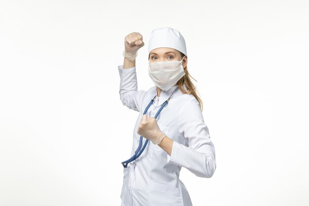 Vue de face femme médecin en costume médical blanc et masque comme protection contre le coronavirus sur le mur blanc clair maladie covid- maladie pandémique