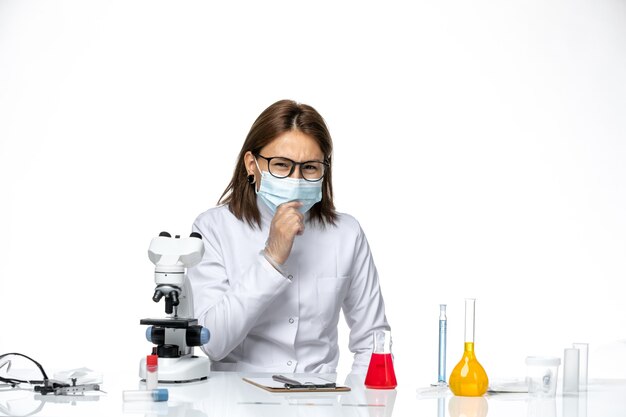 Vue de face femme médecin en costume médical blanc avec masque et gants en raison de covid sur l'espace blanc