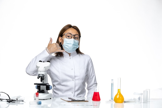 Vue De Face Femme Médecin En Costume Médical Blanc Avec Masque Et Gants En Raison De Covid Posant Sur L'espace Blanc