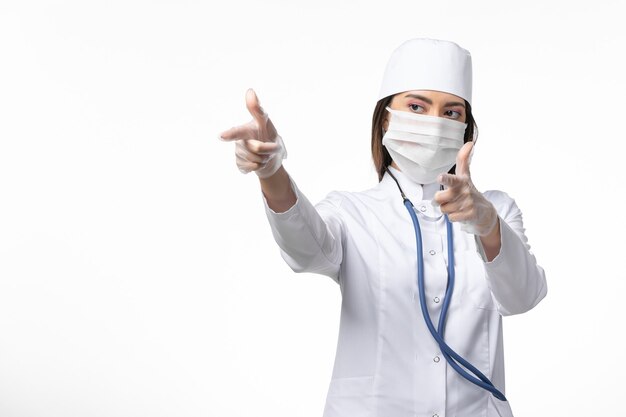 Vue de face femme médecin en costume médical blanc avec un masque en raison d'un coronavirus sur un mur blanc clair maladie pandémique covid-