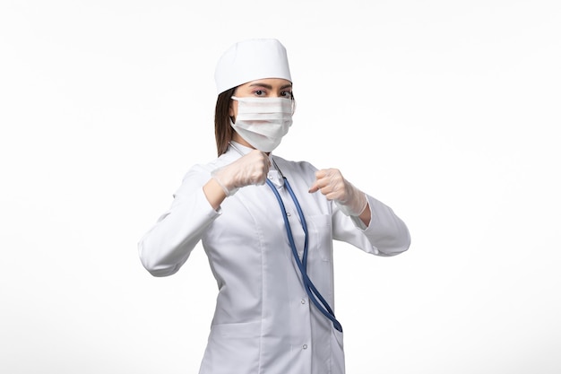 Vue De Face Femme Médecin En Costume Médical Blanc Avec Un Masque En Raison D'un Coronavirus Sur Le Mur Blanc Maladie Maladie Virus Pandémique Covid