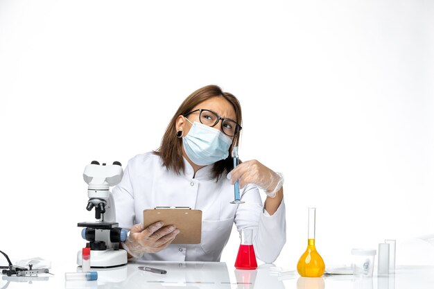 Vue de face femme médecin en costume médical blanc avec masque en raison de covid en processus de travail sur l'espace blanc