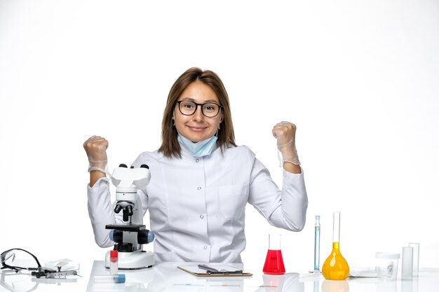 Vue de face femme médecin en costume médical blanc et masque en raison de covid souriant sur l'espace blanc