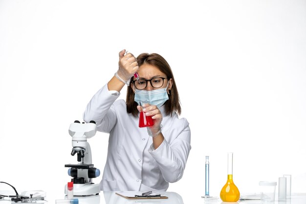 Vue de face femme médecin en costume médical blanc avec masque en raison de covid travaillant avec des solutions sur l'espace blanc