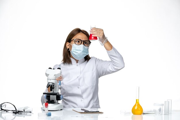 Vue de face femme médecin en costume médical blanc avec masque en raison de covid travaillant avec des solutions sur l'espace blanc