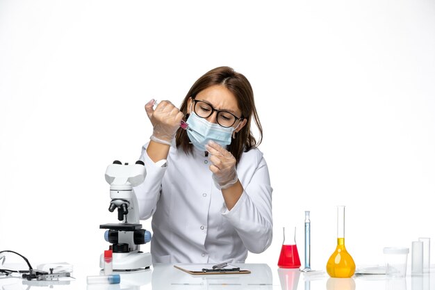 Vue de face femme médecin en costume médical blanc avec masque en raison de covid travaillant avec des solutions sur l'espace blanc