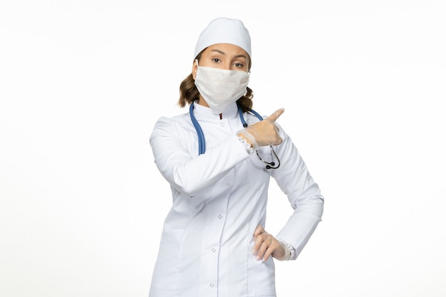 Vue de face femme médecin en costume médical blanc et avec masque en raison du coronavirus sur le mur blanc maladie à virus pandémique covid