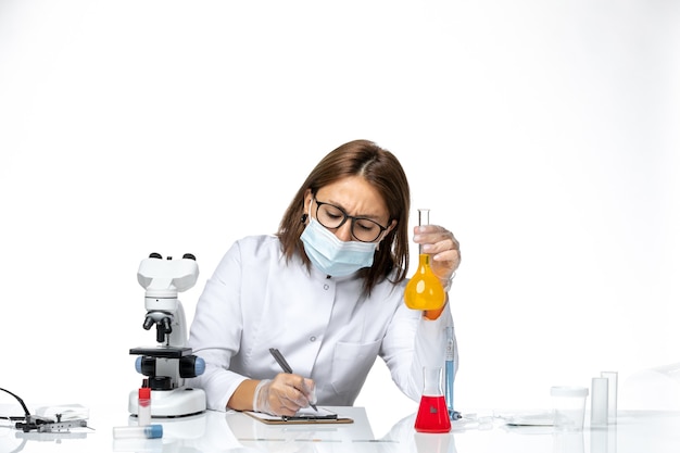 Vue de face femme médecin en costume médical blanc avec masque en raison de l'écriture covid sur un espace blanc clair