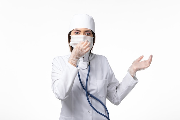 Vue de face femme médecin en costume médical blanc avec un masque en raison de la pandémie sur la maladie du mur blanc de la médecine de la santé pandémique covid-